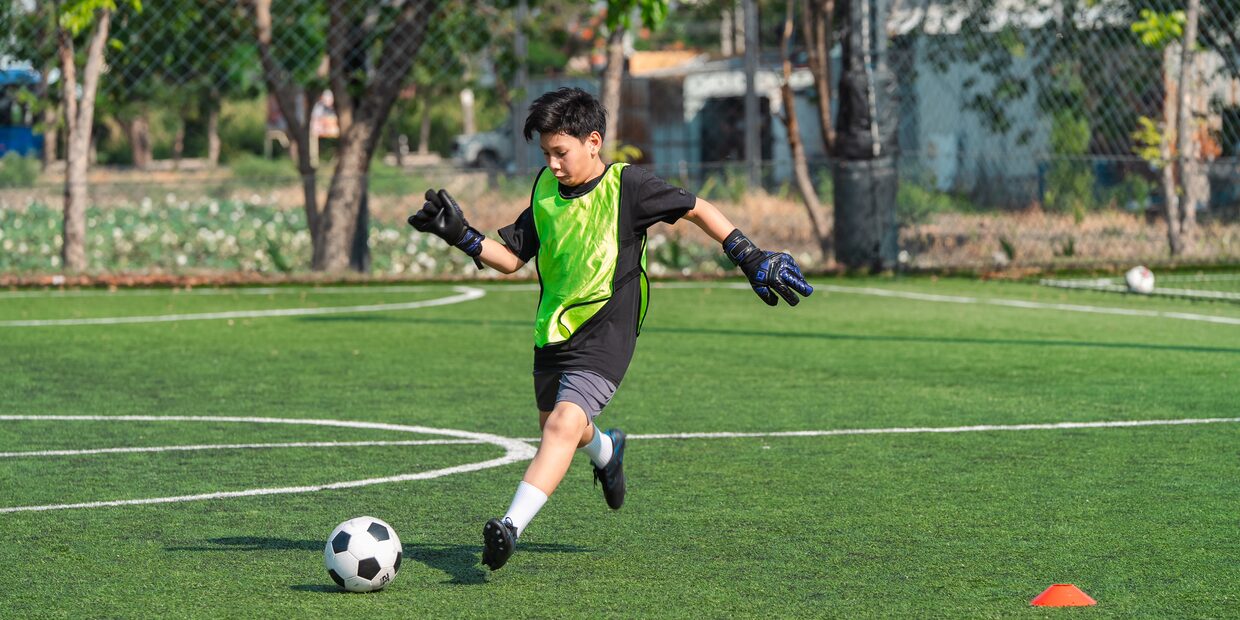 A boy in a green bib striking a ball on an otherwise empty pitch.