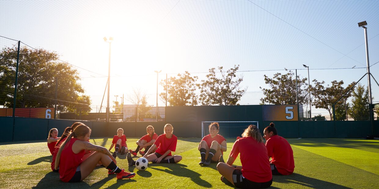 A team sitting together on the grass in front of a goal, the low sun behind them.
